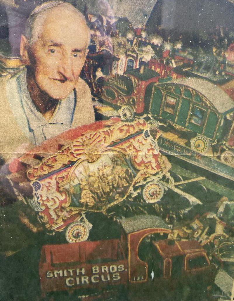 1980 Milo sitting in his living room amongst his 40 carved Golden Age circus wagons of the Smith Brothers Circus - Milo is holding the “Pawnee Bill” wagon, one of his favorite wagons