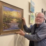 Guest artist Dick Foster hangs one of his oil paintings at Micropolis Gallery