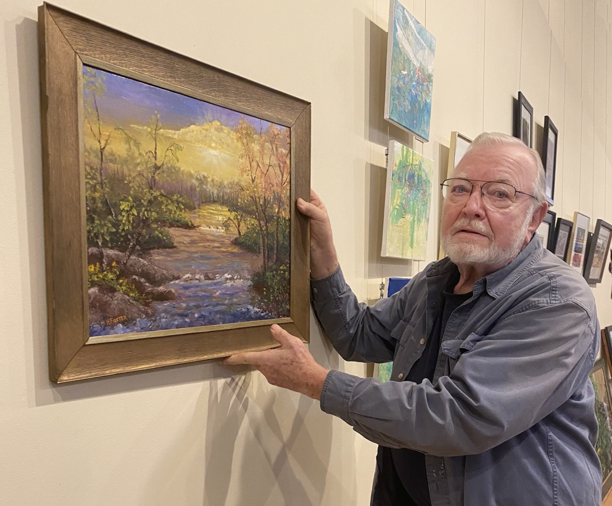 Guest artist Dick Foster hangs one of his oil paintings at Micropolis Gallery